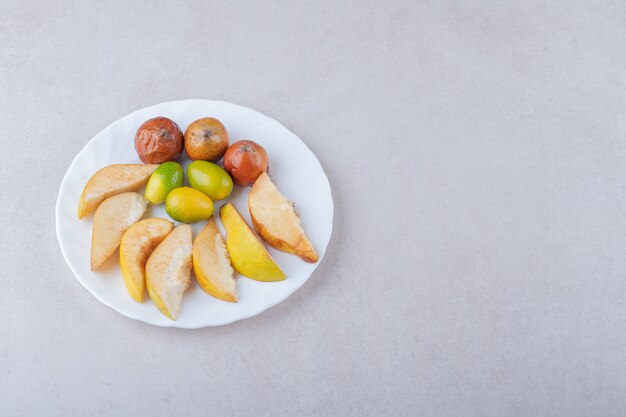 Kweepeer, mispels en kumquats op plaat op marmeren tafel.