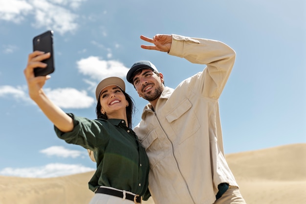 Gratis foto laag hoekpaar dat selfie in woestijn neemt