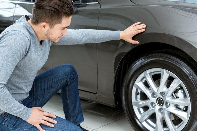 Laatste controle Horizontaal portret van een man die banden controleert op zijn nieuwe auto