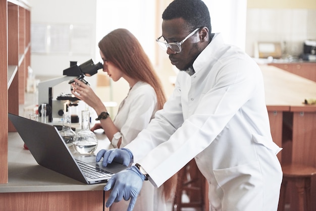 Lab-assistent met microscoop laboratoriumglaswerklamp met chemicaliën.