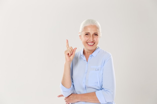 Lachen grijsharige oude dame in blauw shirt, wijzend met de vinger naar boven