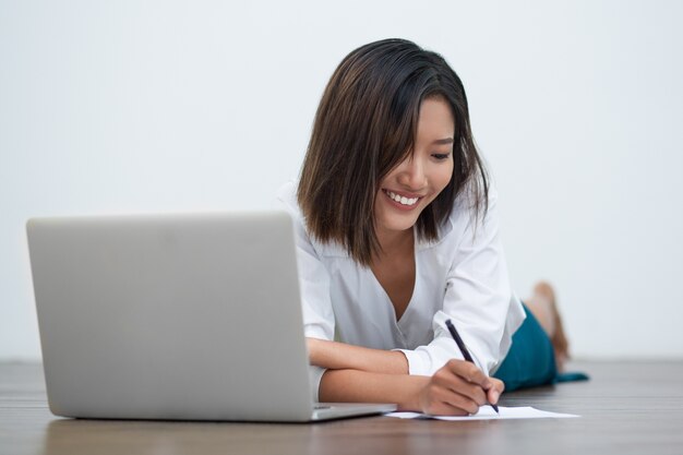 Lachend Aziatische Schrijven van de vrouw op vloer met laptop