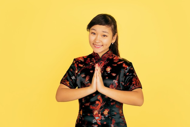 Lachend, bedankt schattig. Gelukkig Chinees nieuwjaar. Aziatisch jong meisje portret op gele achtergrond. Vrouwelijk model in traditionele kleding ziet er gelukkig uit. Viering, menselijke emoties. Copyspace.