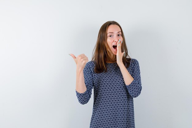 Lachend meisje dat terug met haar linkervinger op witte achtergrond toont