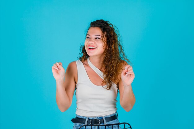 Lachend meisje kijkt naar links door haar vuisten op te heffen op een blauwe achtergrond