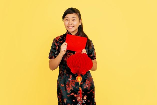 Lachend met lantaarn en envelop. Gelukkig Chinees Nieuwjaar 2020. Portret van een Aziatisch jong meisje op gele achtergrond. Vrouwelijk model in traditionele kleding ziet er gelukkig uit. Copyspace.