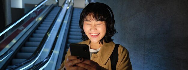 Gratis foto lachend schattig koreaans meisje op de roltrap die met mobiele telefoon naar de metro of metro gaat