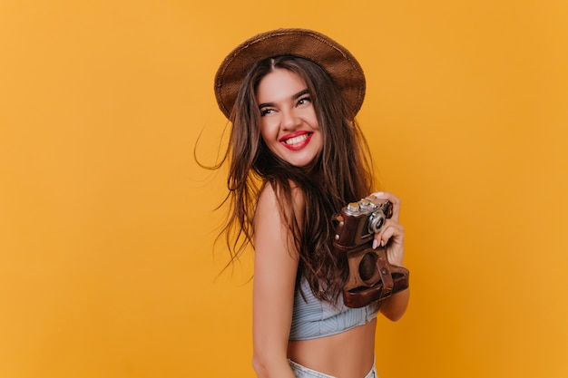 Lachend vrolijk meisje in hoed genieten van fotoshoot op gele ruimte