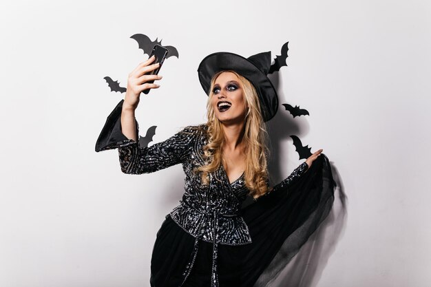 Lachend zorgeloos meisje dat selfie maakt met halloween-vleermuizen Studioportret van een aangename jonge heks die danst op een feestje