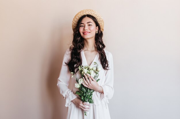 Lachende Aziatische vrouw met witte bloemen. Vooraanzicht van Japanse vrouw in strohoed poseren met boeket.