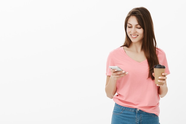 Lachende brunette vrouw poseren in de studio met haar telefoon en koffie