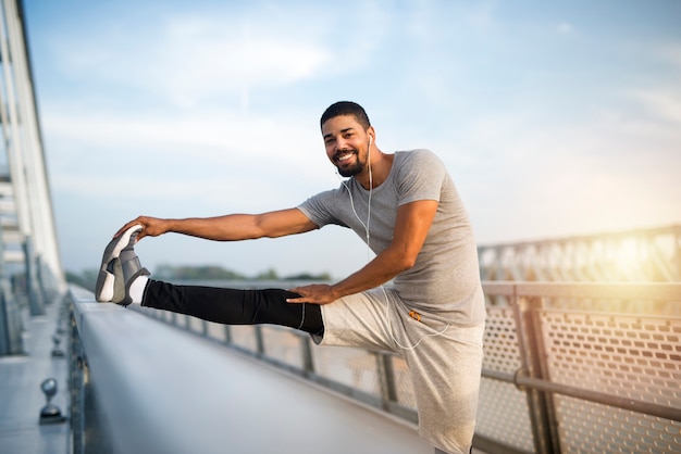 Lachende fit sportieve man warming-up voor de opleiding Afro-Amerikaanse atleet zijn benen strekken voordat u gaat hardlopen.