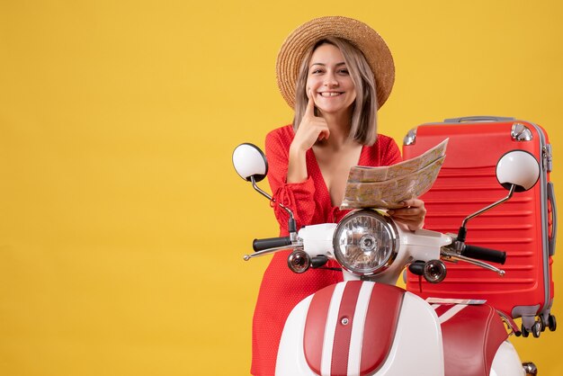 lachende jonge dame in rode jurk met kaart in de buurt van bromfiets