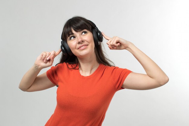 lachende jonge dame, luisteren naar muziek via oortelefoons in ontworpen t-shirt in goed humeur met lang haar op wit