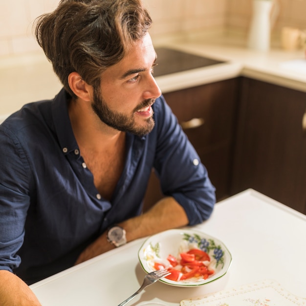 Gratis foto lachende jonge man zit met slakom