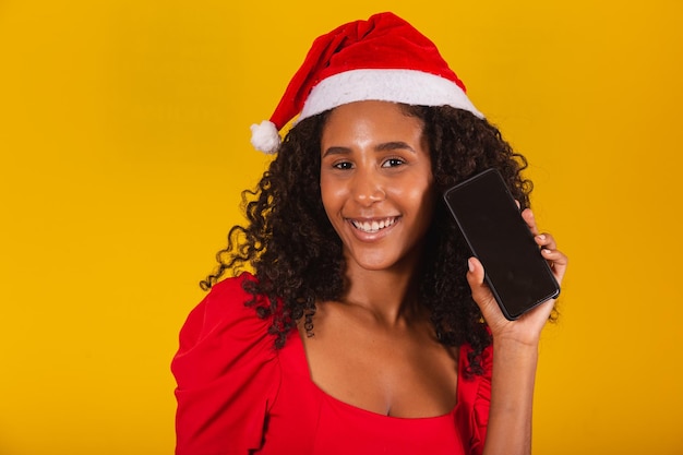 Lachende jonge santa vrouw in kerstmuts met mobiele telefoon met leeg leeg scherm geïsoleerd op gele achtergrond.