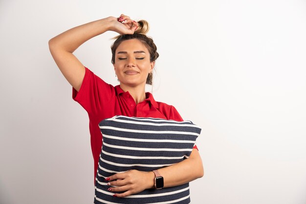 Lachende jonge vrouw knuffelen een kussen op witte achtergrond.