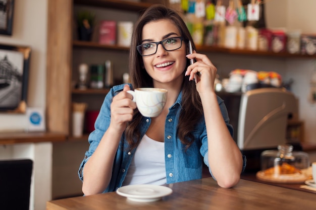 Lachende jonge vrouw praten via de mobiele telefoon in café
