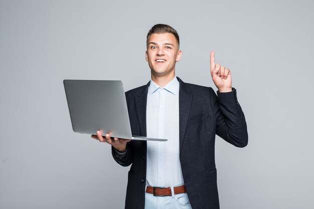 Lachende jongeman poseren met laptop telefoon gekleed in een donkere jas in studio geïsoleerd op een grijze muur