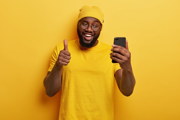 lachende knappe man met bril poseren met zijn telefoon