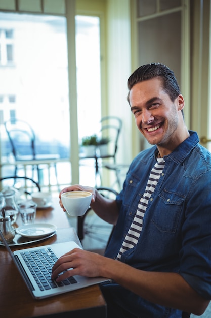 Lachende man met behulp van laptop, terwijl met koffie in cafÃ ©