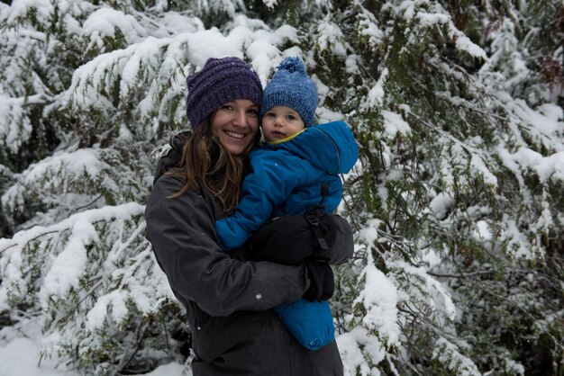 Lachende moeder met zoon tegen sneeuw bedekte bomen