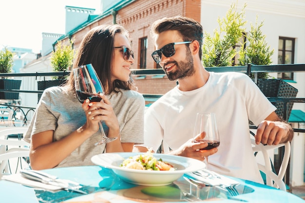 Lachende mooie vrouw en haar knappe vriendje Gelukkige vrolijke familie Paar juichen met glazen rode wijn op hun date in restaurant Ze drinken alcohol in veranda café in de straat