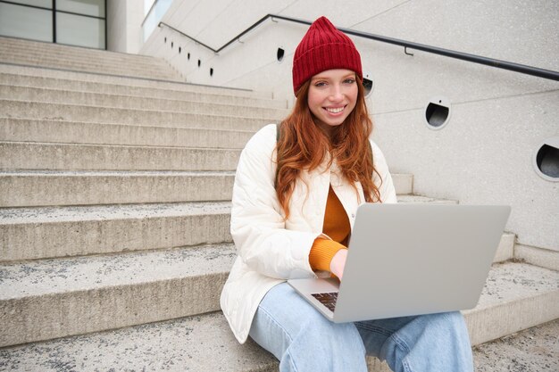 Lachende roodharige meisje jonge vrouw typen op laptop toetsenbord buiten zitten op trappen met computer