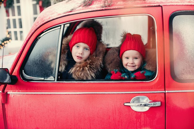 Lachende schattige winterjongen en meisjeskinderen in rode hoed die in de auto zitten en plezier hebben