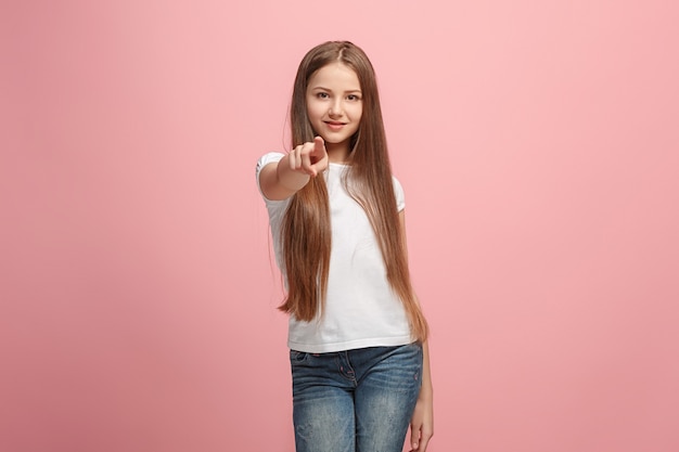 Lachende tiener meisje wijst naar camera, halve lengte close-up portret op roze studio achtergrond.