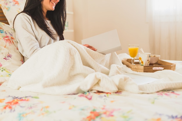 Lachende vrouw die een boek in het bed