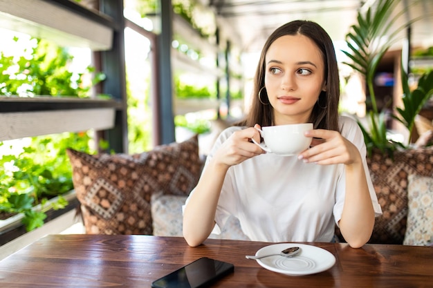 Lachende vrouw in een goed humeur met kopje koffie zitten in café.