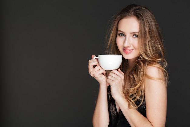 Lachende vrouw koffie drinken over donkere muur