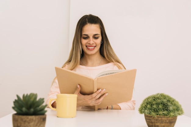 Gratis foto lachende vrouw leesboek aan tafel