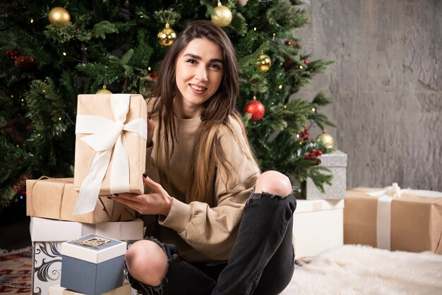 Lachende vrouw liggend op pluizig tapijt met kerstcadeautjes.