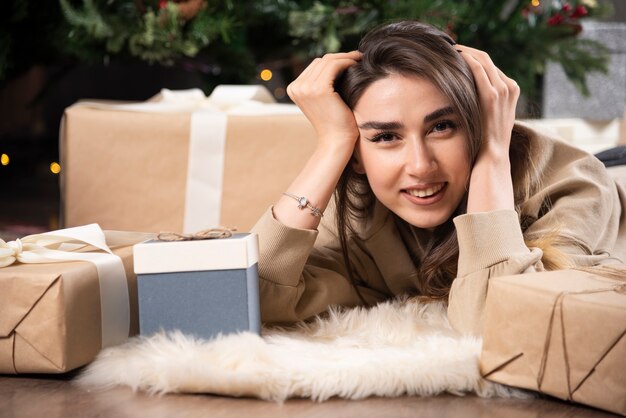 Lachende vrouw liggend op pluizig tapijt met kerstcadeautjes.