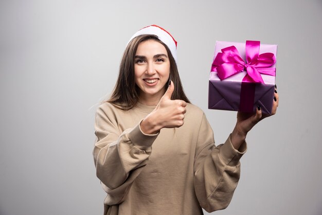 Lachende vrouw met een doos met kerstcadeautjes met een duim.