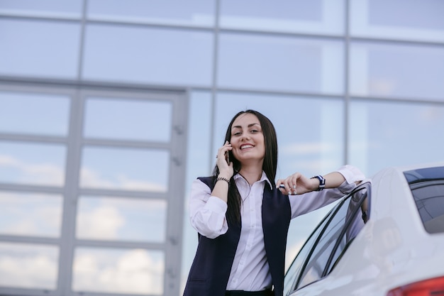 Lachende vrouw met een elleboog op een auto leunt tijdens het gesprek op de telefoon