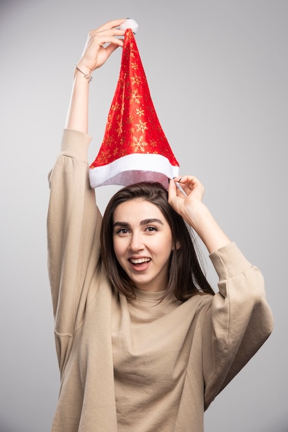 Gratis foto lachende vrouw met kerstmuts overhead op een grijze achtergrond.