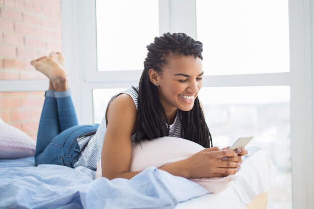 Lachende vrouw netwerken op mobiele telefoon in bed