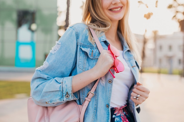 lachende vrouw wandelen in de stad straat in stijlvol oversized denim jasje, met roze lederen rugzak
