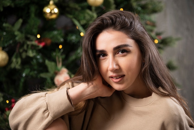 Lachende vrouw zitten en poseren in de buurt van de kerstboom.