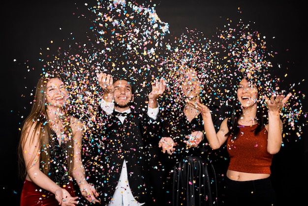 Lachende vrouwen en man in avonddoeken die confetti gooien