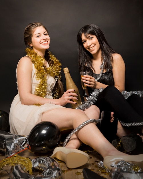 Gratis foto lachende vrouwen in avondkleding met een glas drank en een fles op de vloer