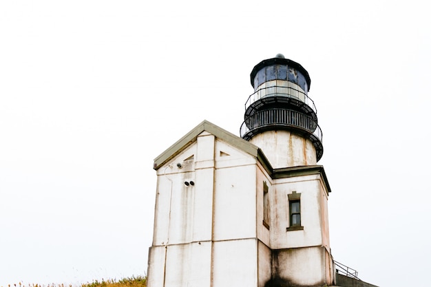 Lage hoek die van een oude vuurtoren met een witte hemel is ontsproten