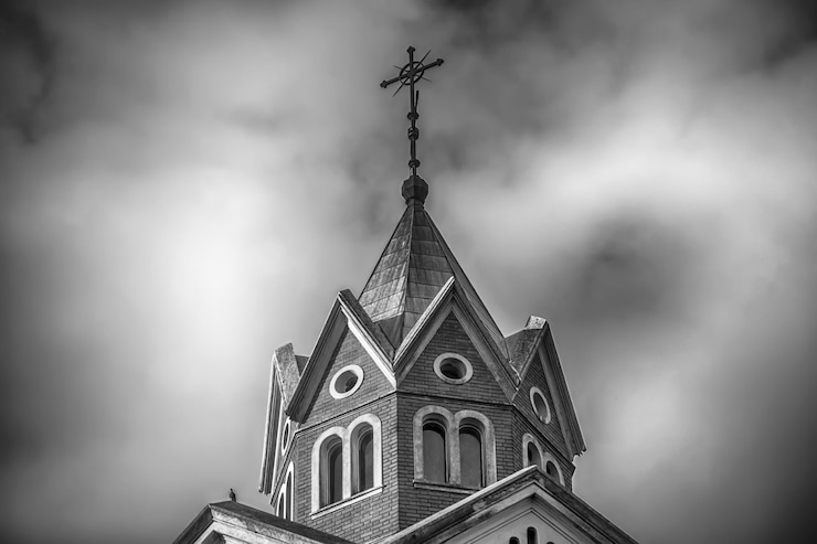 Gratis Foto lage hoek greyscale shot van de top van een christelijke kerk met bewolkte hemel