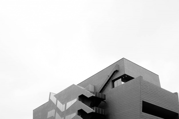 Gratis foto lage hoek greyscale shot van een betonnen modern gebouw geïsoleerd op een witte muur