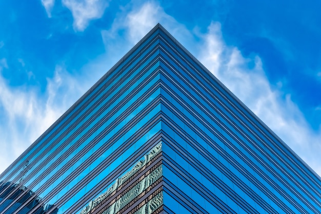 Lage hoek shot van een hoog glazen gebouw onder een blauwe bewolkte hemel