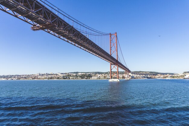 Lage hoek shot van een Ponte 25 de Abril brug over het water met de stad in de verte