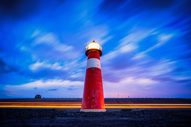 Gratis foto lage hoek shot van een rode en witte verlichte vuurtoren op de weg onder een blauwe en paarse bewolkte hemel